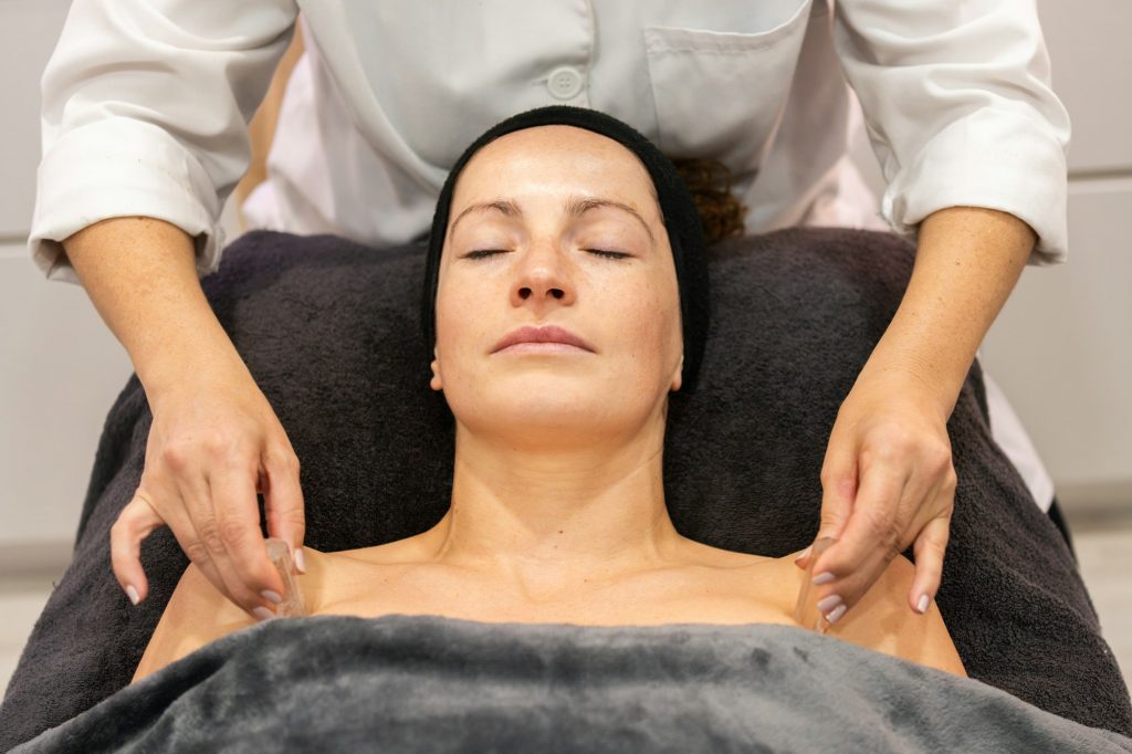 Crop beautician massaging shoulder with ice cube on client in beauty salon