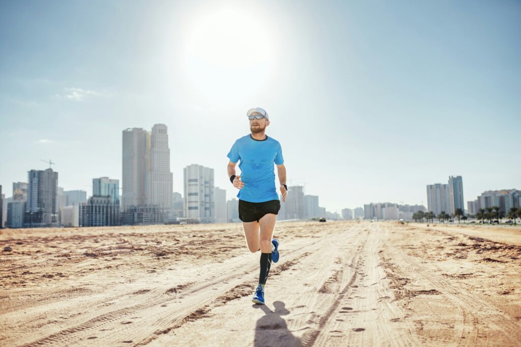 Full length front view of mid adult man running on sand by sky scrapers, Dubai, United Arab Emirates