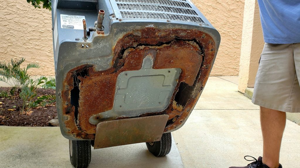 HVAC technician removes a rusted and weathered air conditioner from beach condo to replace with new.
