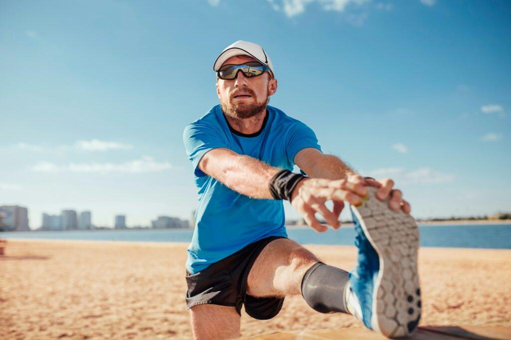 Mid adult man on beach leg raised touching toes stretching foot, Dubai, United Arab Emirates