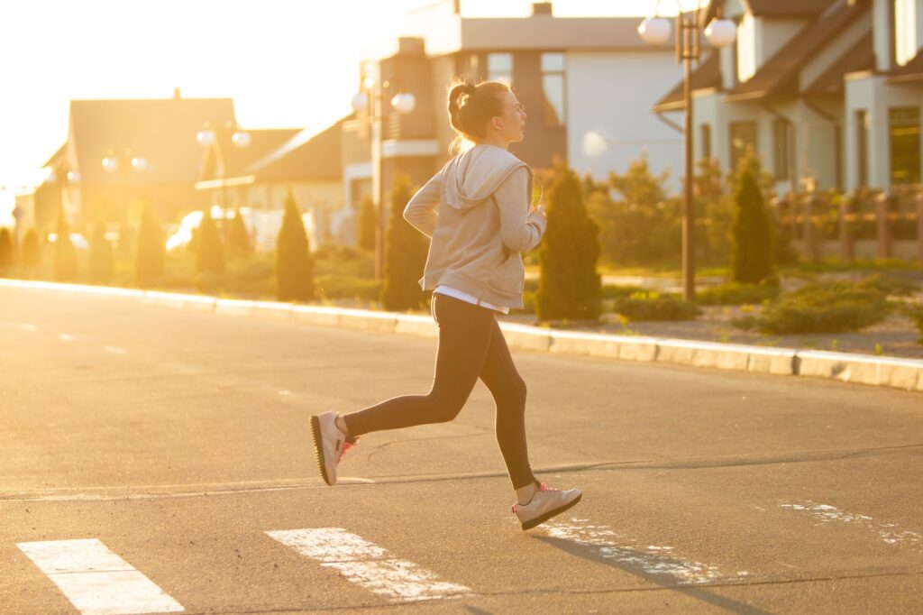 Young female runner, athlete is jogging in the city street in sunshine. Beautiful caucasian woman
