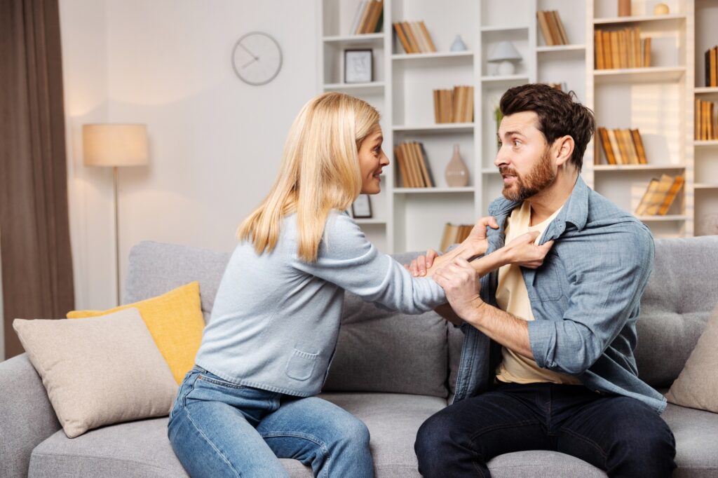 Assistance for household conflicts concept: woman, in anger, attacking her husband on sofa