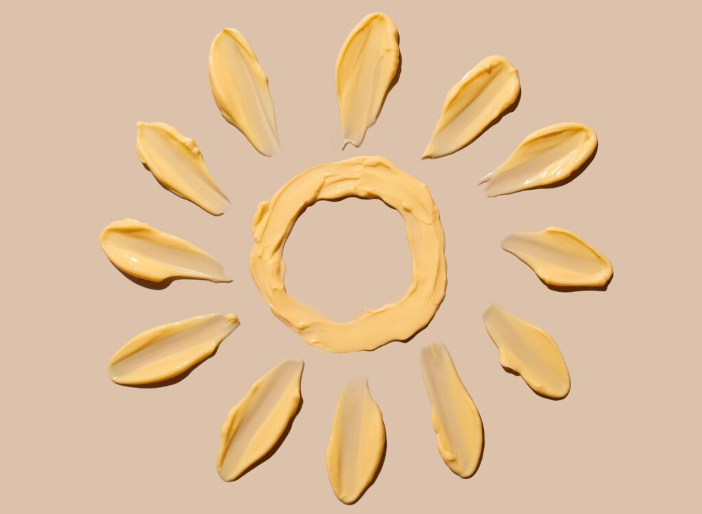 Cosmetic smear of a cream texture in the form of a yellow sun on a beige background. Sunscreen cream