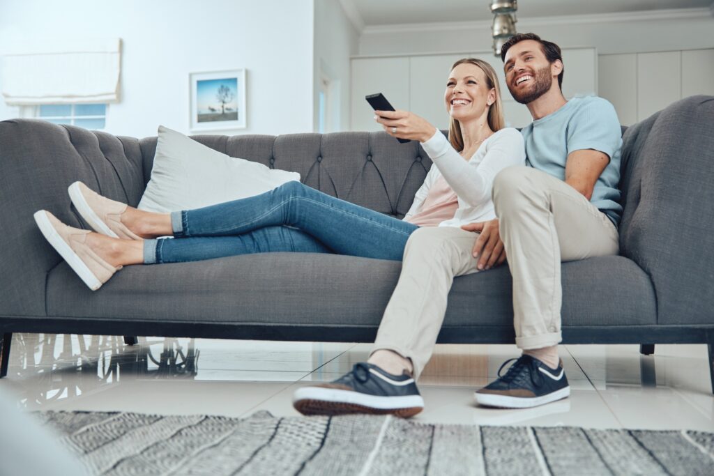 Couple, sofa and relax with tv remote, smile and happiness in home living room for bonding with lov
