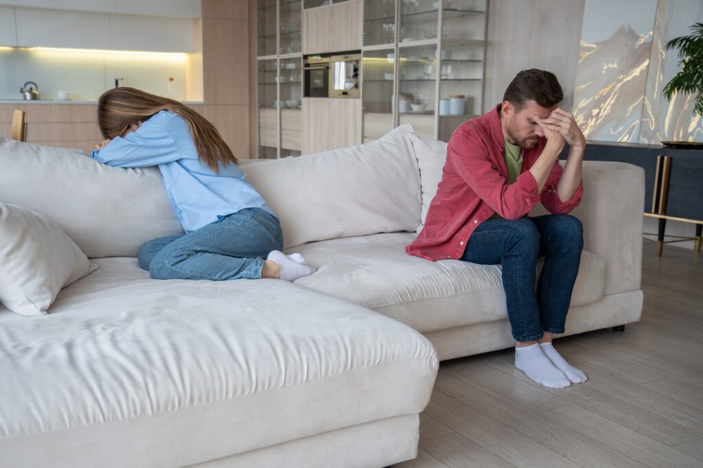 Desperate wife crying, thinking of divorce, and unhappy sad husband sitting in silence after quarrel