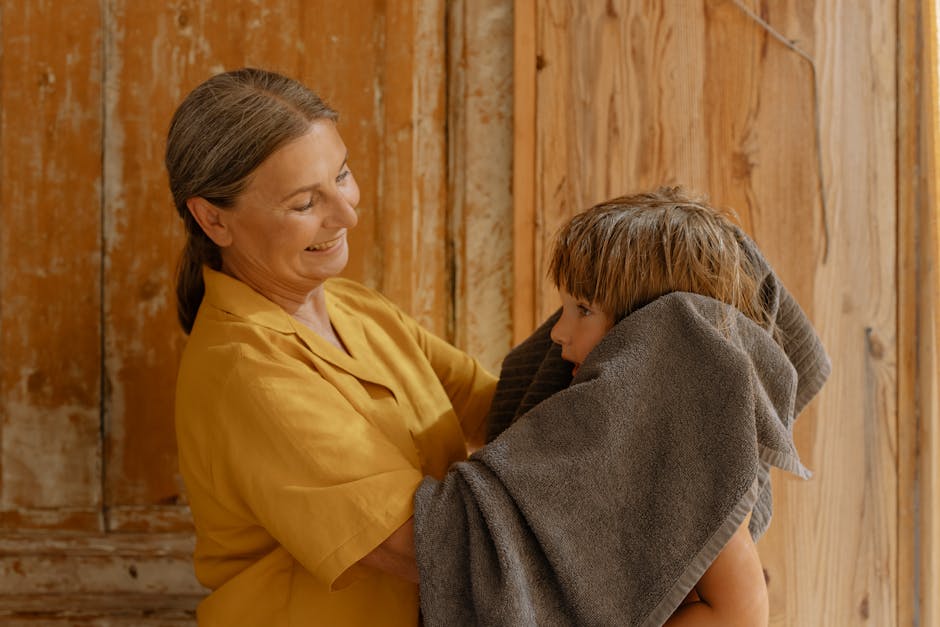 Child bundled up in winter clothes being dried hair by a parent indoors