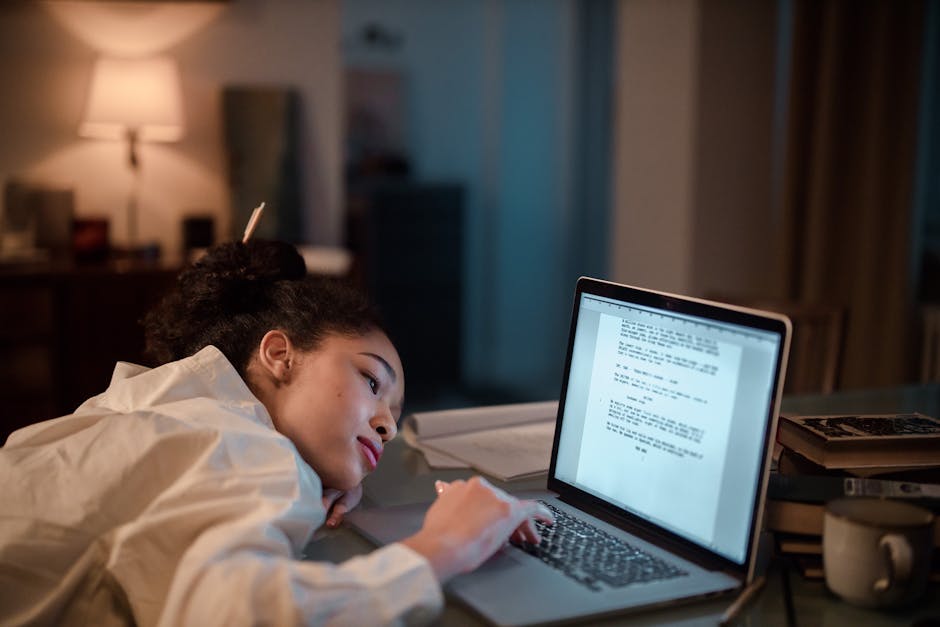 Person studying at a desk with laptop and notebook at night