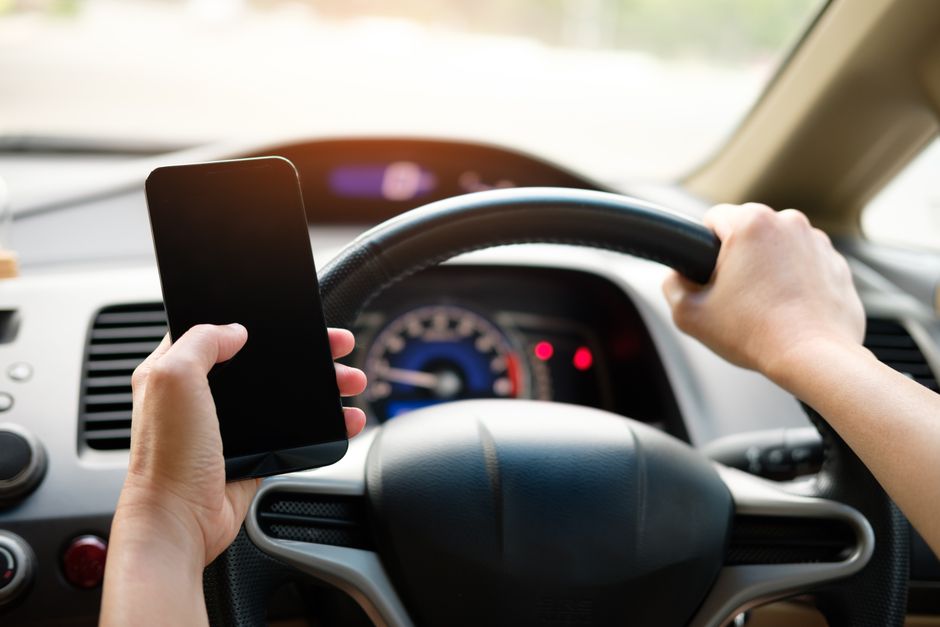 Person distracted by smartphone near a car at a gas station
