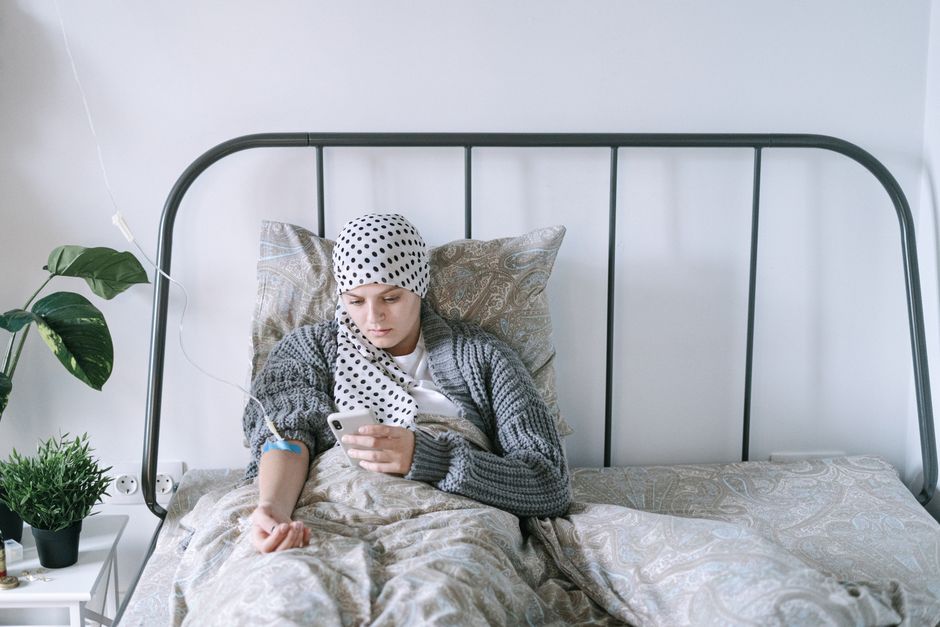 Les smartphones causent-ils vraiment le cancer du cerveau ? Ce que dit VRAIMENT la science en 2026 A woman undergoing chemotherapy checks her smartphone in a hospital bed, symbolizing hope and recovery.