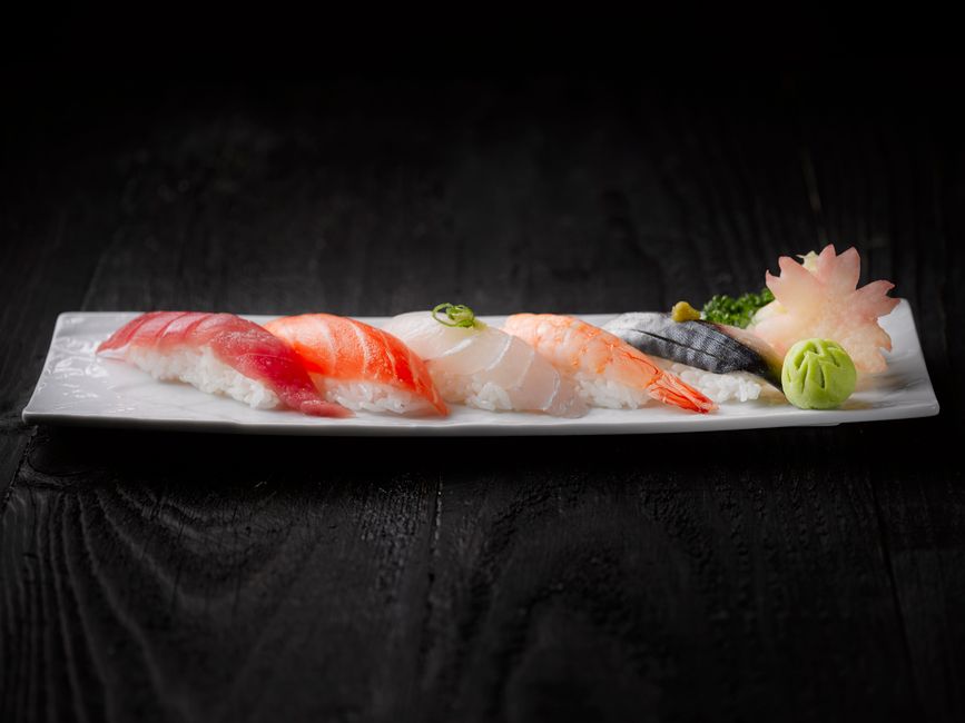 A beautifully arranged sushi platter featuring fresh sashimi on a sleek white plate with wasabi and garnish.