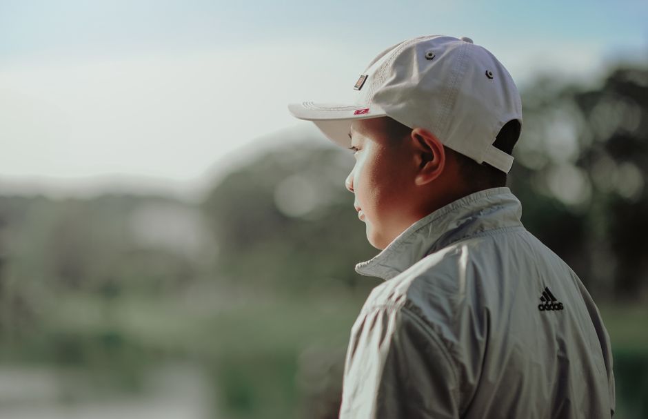 A boy wearing a white cap and jacket looks thoughtfully into the distance outdoors.