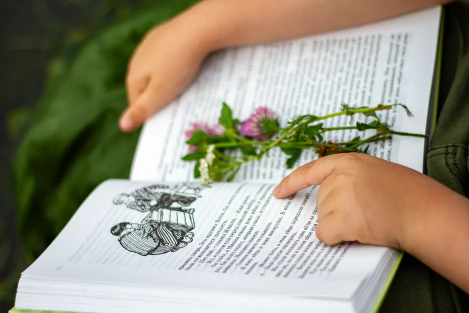 La dyslexie est-elle vraiment un handicap ou un don? A child reading an open book with wildflowers placed on the pages, outdoors.