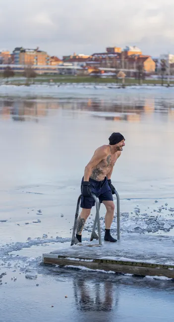A man climbing a ladder from an icy lake after cold water immersion in winter.