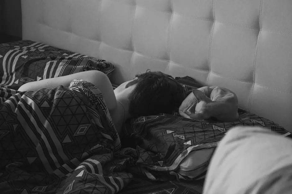 Peut-on vraiment rattraper une nuit blanche? A peaceful black and white photo of a person sleeping in bed with patterned sheets.