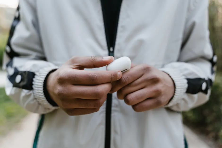 Les écouteurs peuvent-ils vraiment endommager l’audition? A person in a jacket holding a case of wireless earbuds outdoors.