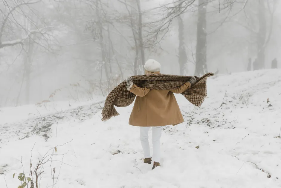 Peut-on attraper un rhume parce qu’on a froid? Le thermomètre face au virus A person in winter attire walking through a snow-covered forest, embracing the cold weather.