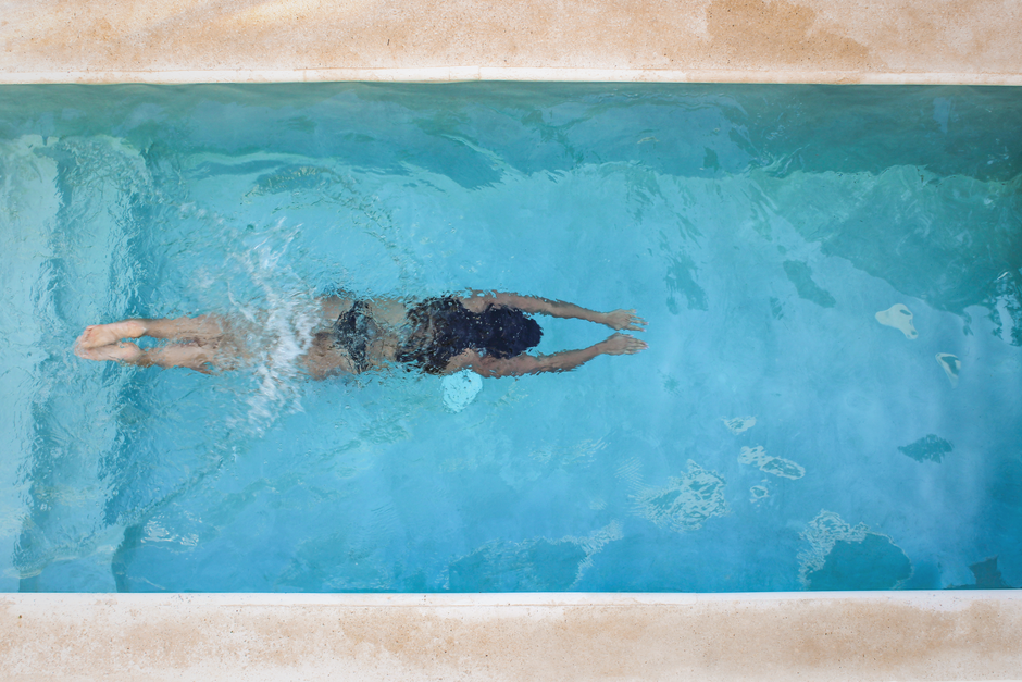 Les bains froids renforcent-ils vraiment l’immunité? A person swimming with strong strokes in a clear blue pool, seen from above.