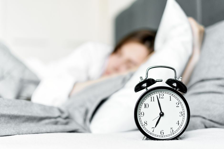 Le sommeil avant minuit compte-t-il vraiment double? A retro alarm clock sits by a sleeping woman in a cozy bedroom setting.