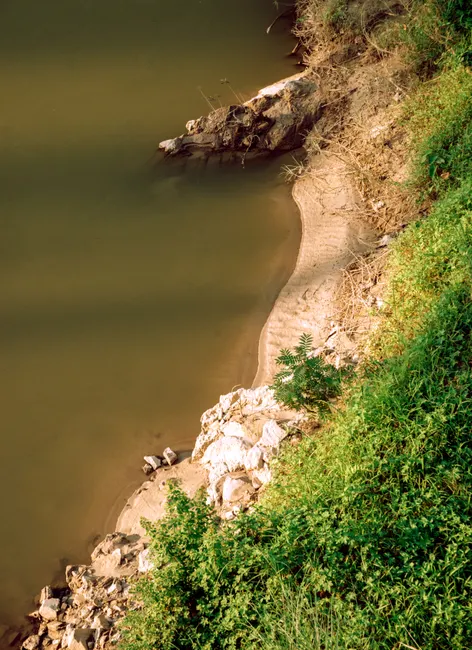 A serene aerial shot of a riverbank with lush greenery and rocky shorelines.