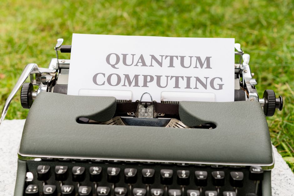 A typewriter with 'Quantum Computing' text outdoors on grass, blending old and new technologies.