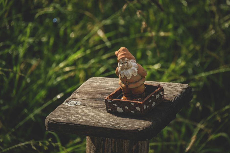 Les nains de jardin ont-ils une vraie signification symbolique? A whimsical garden gnome figurine sits on a rustic wooden pedestal amidst lush greenery.