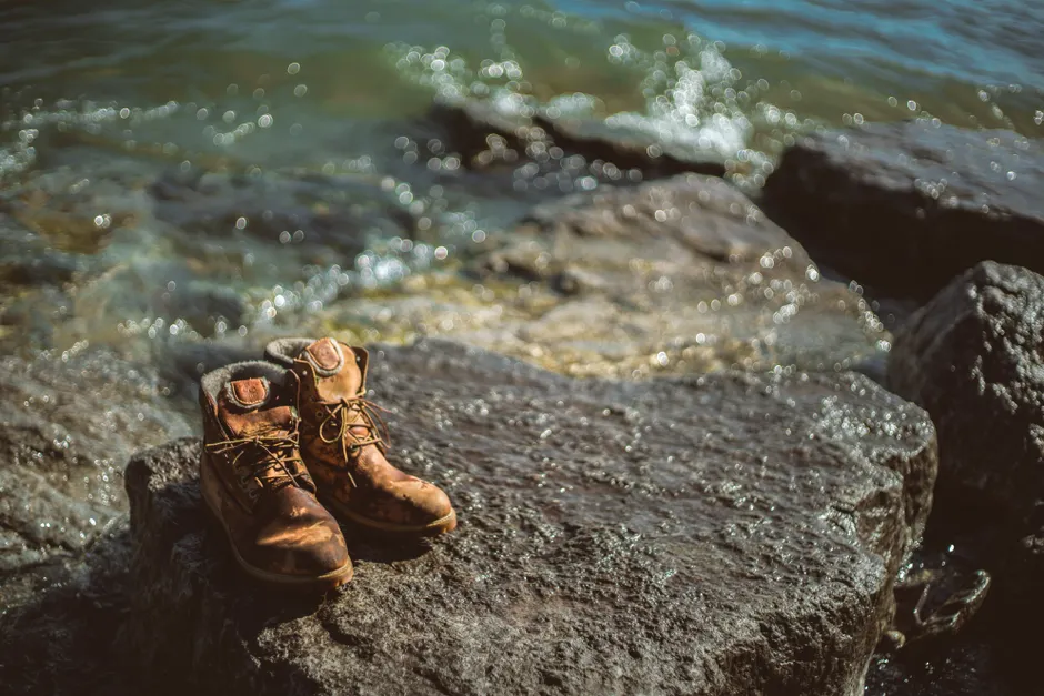 Les sables mouvants existent-ils encore aujourd’hui? Abandoned hiking boots on a rocky shoreline with waves crashing in.