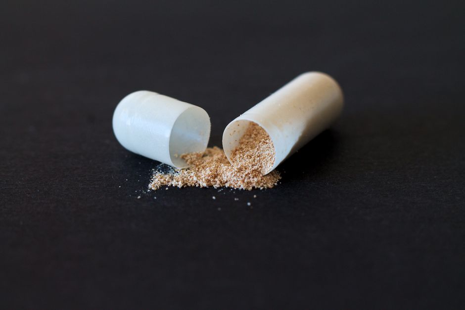 Close-up of a split capsule with powder spilling on a dark surface, symbolizing medicine and health.