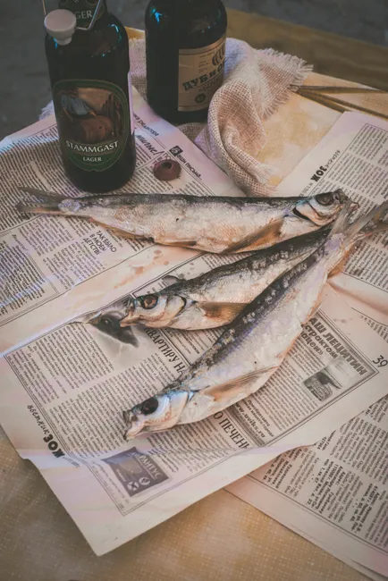 Close-up of dried fish placed on newspaper with beer bottles in the background.