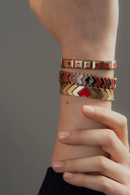 Close-up of fashionable geometric bracelets in red and gold hues on a woman's wrist.