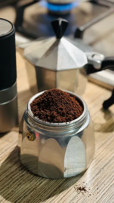 Close-up of fresh ground coffee in a moka pot by a stove.