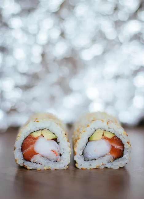 Close-up of savory salmon sushi rolls with avocado and rice on a wooden table, ideal for food enthusiasts.