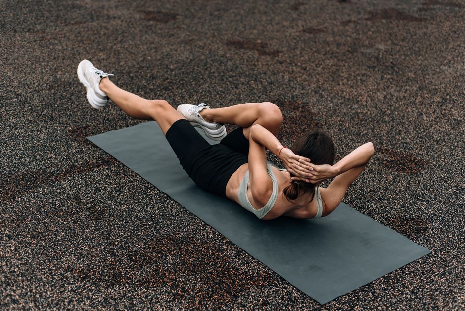 Les abdominaux font-ils vraiment perdre la graisse du ventre? Fit woman doing a bicycle crunch on a mat outdoors, emphasizing core strength and fitness.