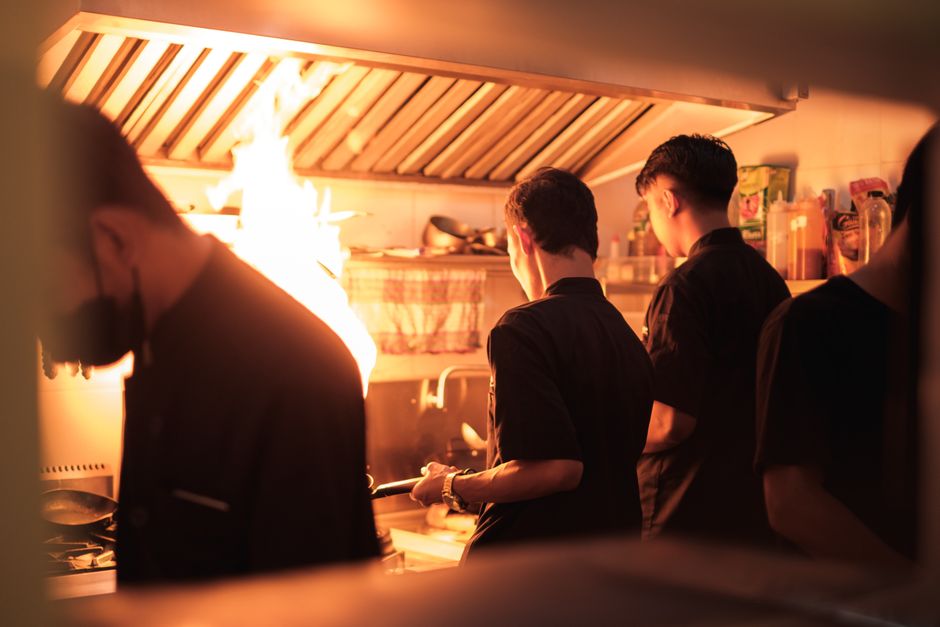 Les chefs cuisiniers sont-ils vraiment plus stressés que les autres travailleurs? Professional chefs working in a busy industrial kitchen with visible flames.