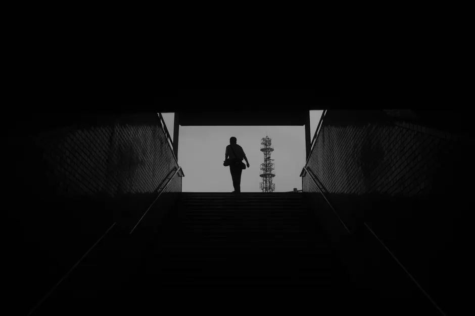 Silhouette of a person emerging from a dark tunnel with a tall structure in the background.