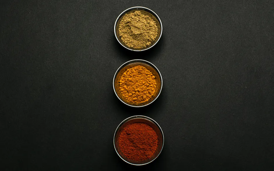 Le curcuma est-il vraiment efficace contre l’inflammation? Top view of assorted spice powders in metal bowls showcasing vibrant colors against a dark background.