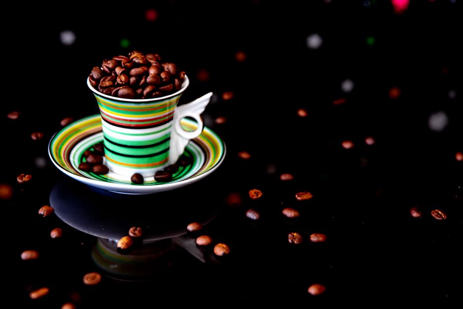 Le café torréfié contient-il vraiment du furane? Vibrant striped cup overflowing with dark roasted coffee beans against a black background.