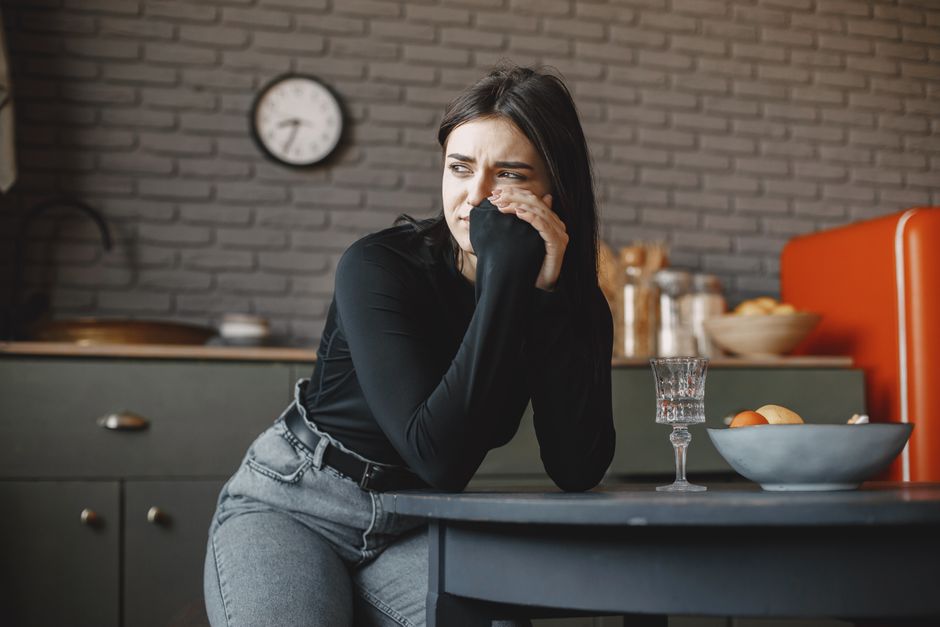Le jeûne intermittent est-il vraiment efficace? Young woman in a pensive mood, sitting indoors with a clock in the background.