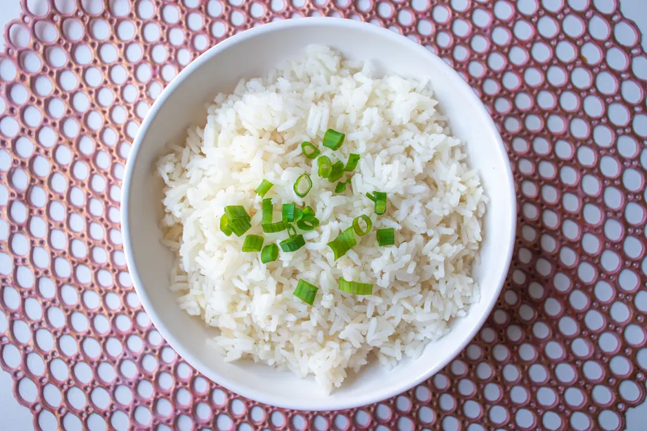 Réchauffer du riz est-il vraiment risqué? A bowl of cooked white rice garnished with green onions, perfect for culinary presentations.