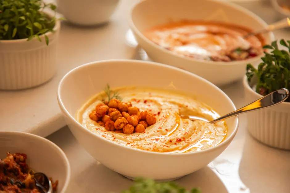 Le houmous est-il vraiment un plat sain? A close-up of creamy hummus with spiced chickpeas and herbs in a bowl, perfect for healthy eating.