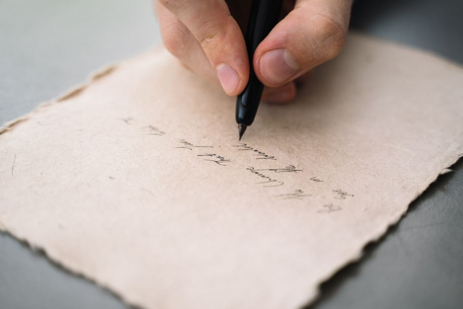 L’écriture manuscrite disparaîtra-t-elle avec le numérique? Le recul n’est pas l’extinction A close-up view of a person's hand writing with a black pen on textured paper.