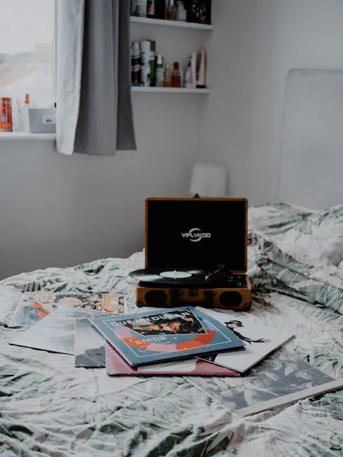 A cozy bedroom scene with a vintage record player and vinyl records on a bed.