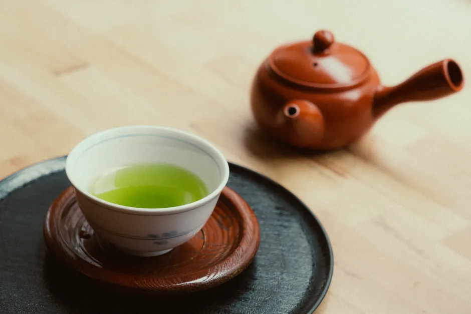 Le thé vert fait-il vraiment maigrir? Le verdict des études A cup of vibrant green tea and a clay teapot on wooden surface, capturing a calming essence.