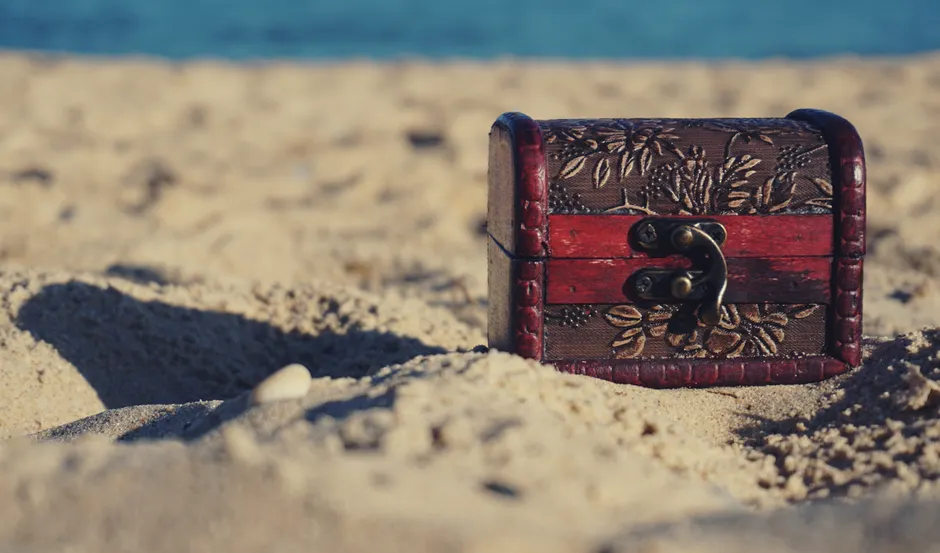 Les pirates enterraient-ils vraiment tous leurs trésors? A decorative treasure chest sits on a sunny beach, invoking mystery and adventure.