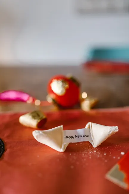A fortune cookie with a 'Happy New Year' message on a festive table setting.