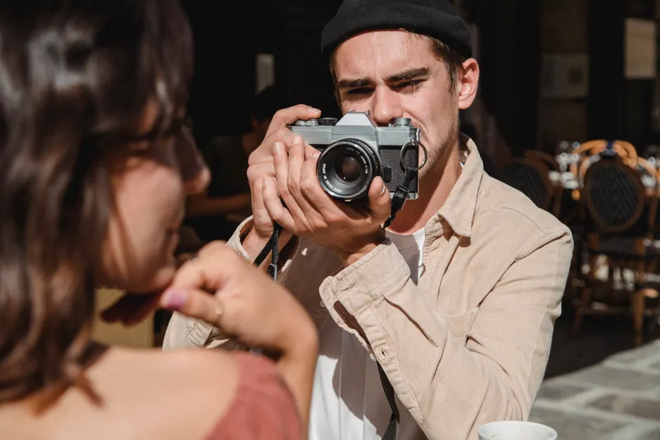 Les tests de personnalité sont-ils vraiment fiables? A man taking a photo of a woman with a vintage camera in an outdoor cafe setting.