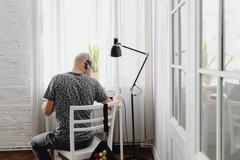 La musique rend-elle vraiment plus productif? Le verdict des études A man wearing headphones works at a desk by a window in a bright indoor setting.