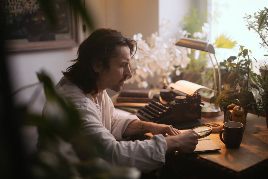 L’IA peut-elle vraiment écrire un roman convaincant? A man with long hair examines a manuscript using a magnifying glass in a cozy study.