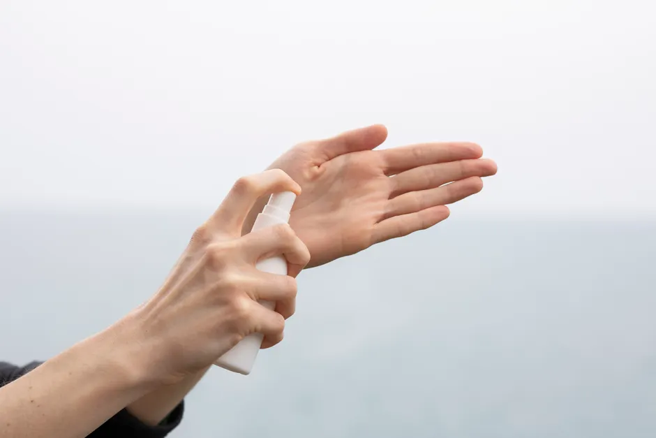 A person using hand sanitizer spray by the sea, promoting hygiene and cleanliness.
