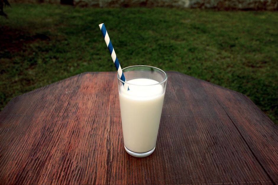 Le lait est-il vraiment indispensable aux os? A refreshing glass of milk with a straw on a wooden table set outdoors, perfect for a healthy break.