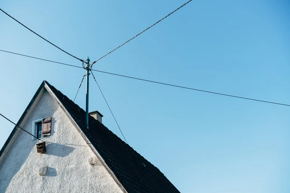 A suburban house's rooftop with visible power lines against a clear blue sky, conveying modern infrastructure.